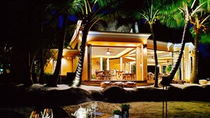 A beachfront hotel with a spacious lobby, palm trees, and a dining area with a table set for two.