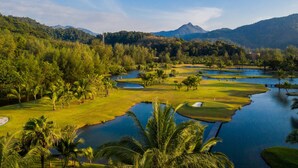 A golf course with water hazards, palm trees, and a mountainous backdrop.