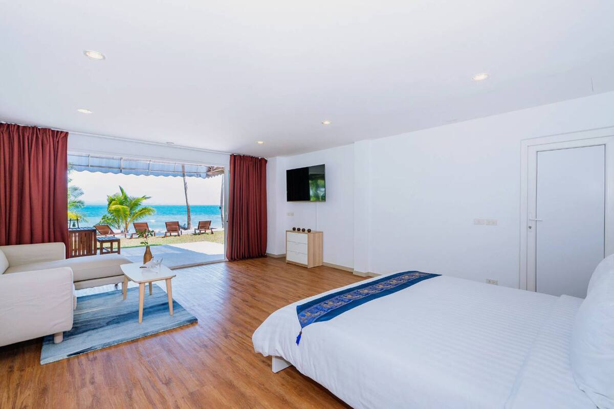 Hotelkamer met een groot bed, een sofa, een kleine tafel en een televisie. De kamer heeft een houten vloer en uitzicht op het strand en de zee.