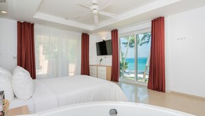 Een slaapkamer met een groot bed, een plafondventilator, een televisie en uitzicht op de oceaan.