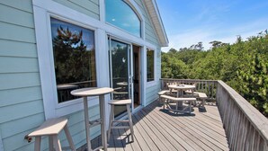 Um deck de madeira com área de estar externa e uma grande janela com vista para uma área arborizada.