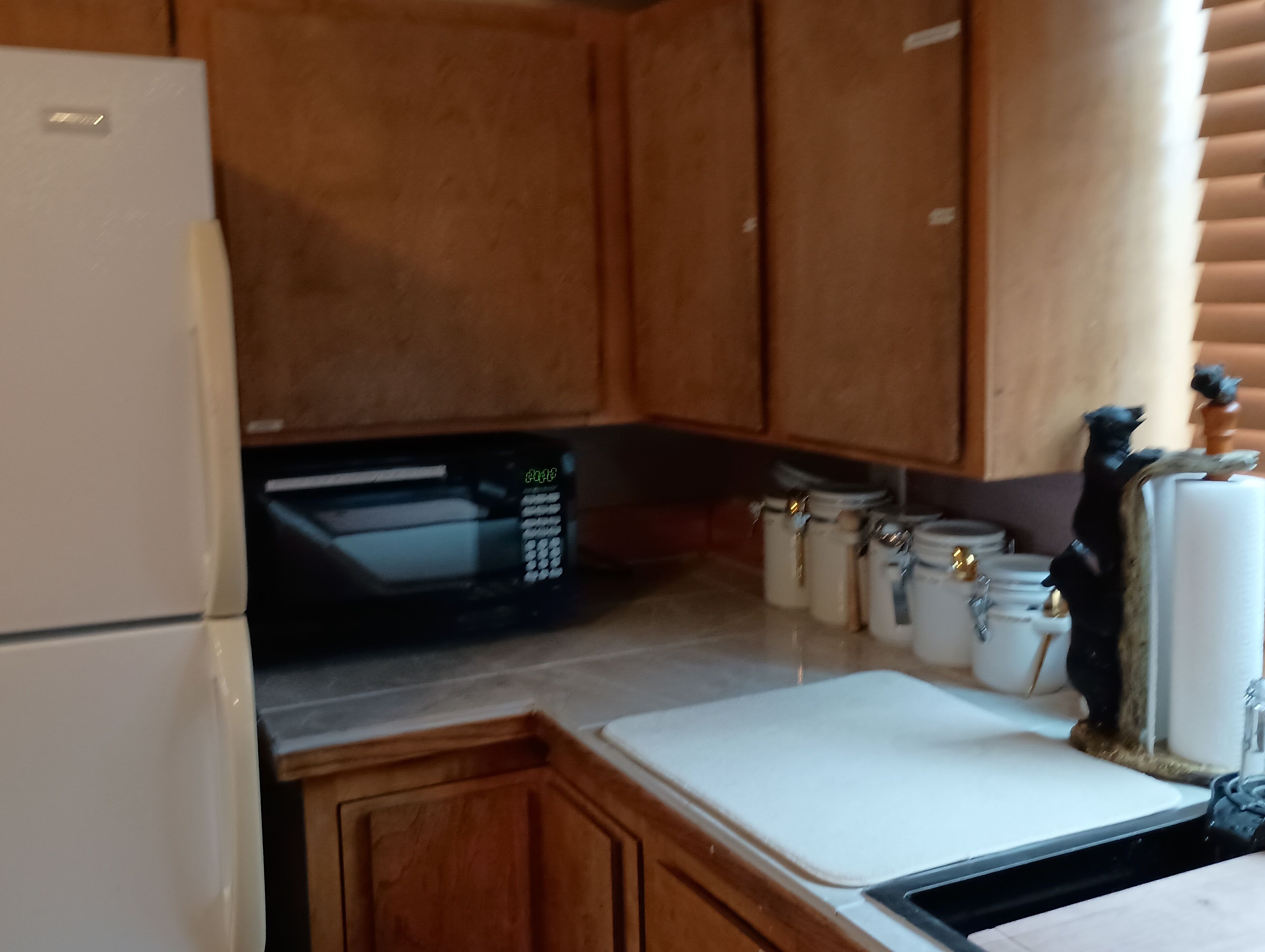 Une cuisine de taille réduite, dotée de meubles en bois, d’un four à micro-ondes et d’un petit plan de travail.