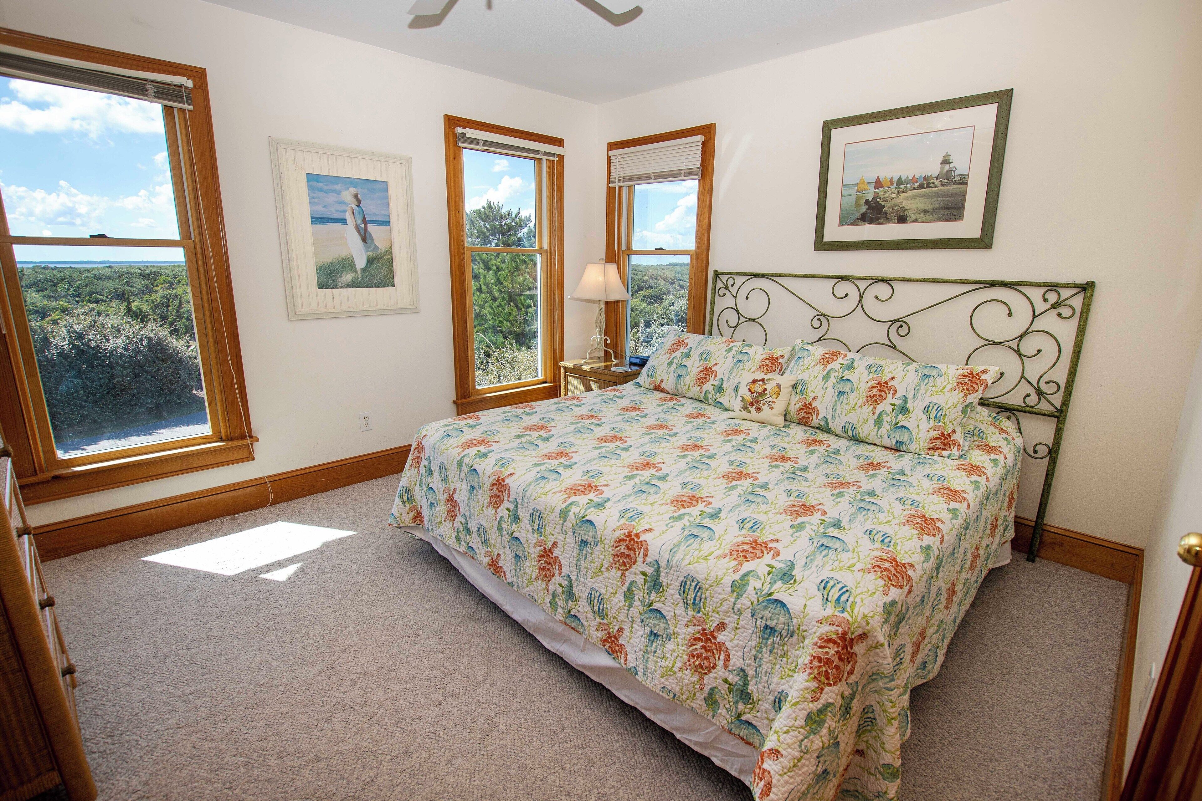A bedroom with a bed, two windows, a nightstand, and a lamp.