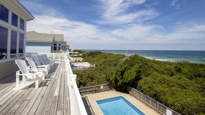 Ett trädäck med solstolar med utsikt över en pool och havet.