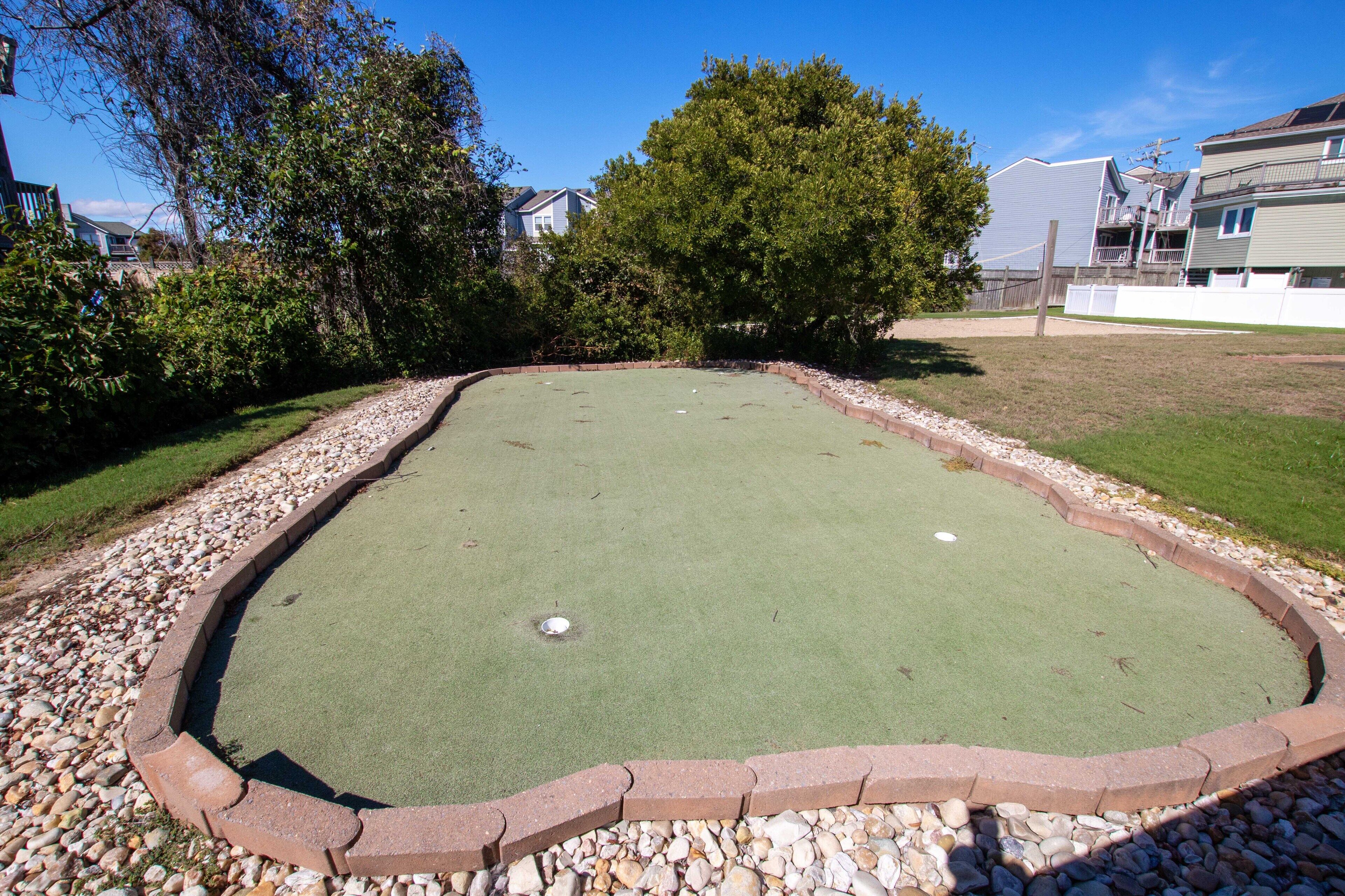 Un campo de croquet verde con borde de ladrillo, rodeado por un sendero de grava y árboles.