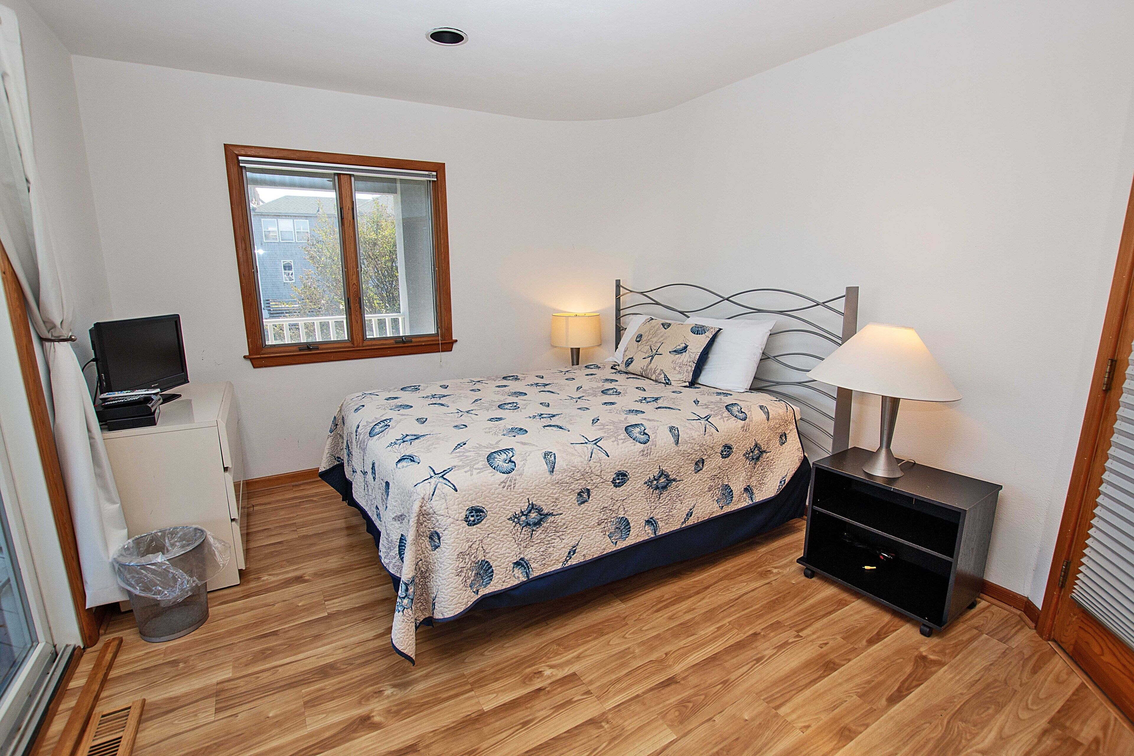 A bedroom with a bed, bedside table, lamp, and a small desk with a computer.