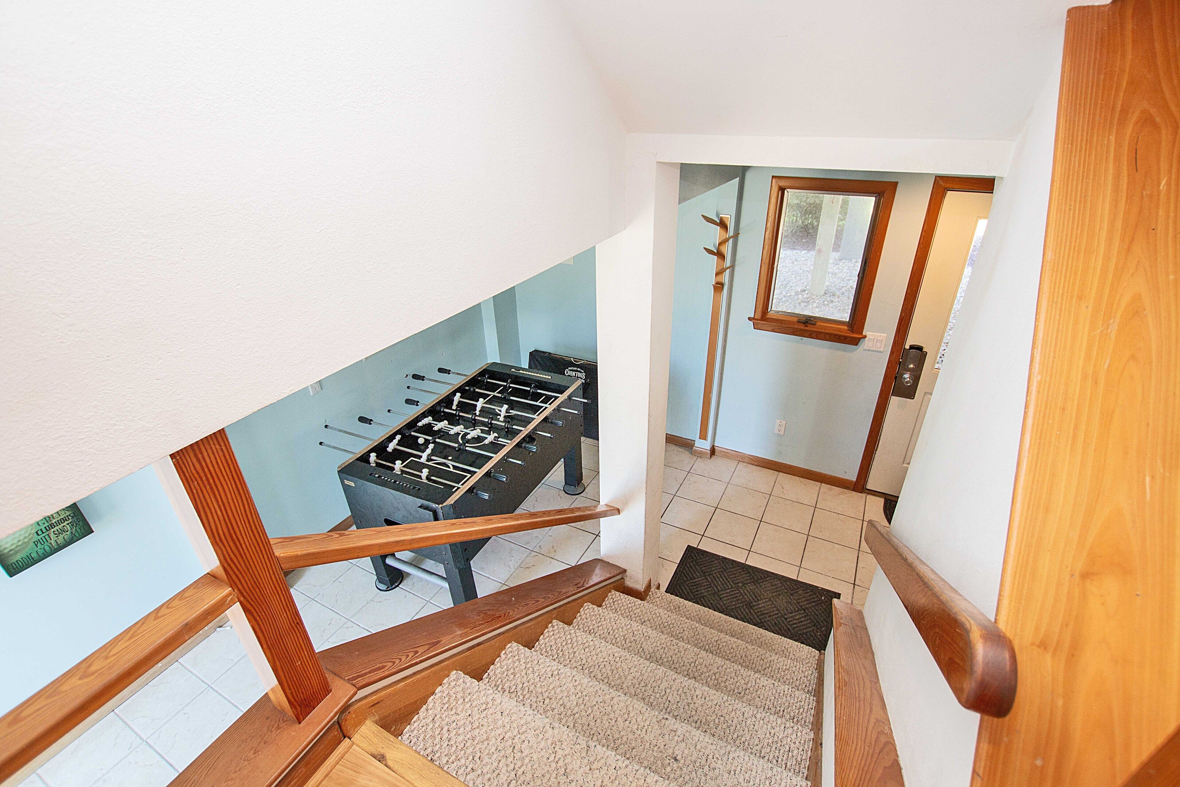 A staircase with wooden handrails leading to a room with a foosball table.