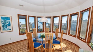 A dining area with a round glass table, wooden chairs with blue cushions, and large windows offering a view of the neighborhood. - Semi-Oceanfront, Private Pool, Hot Tub, Close to Beach Access, GF2, Touch of Grey (Duck)