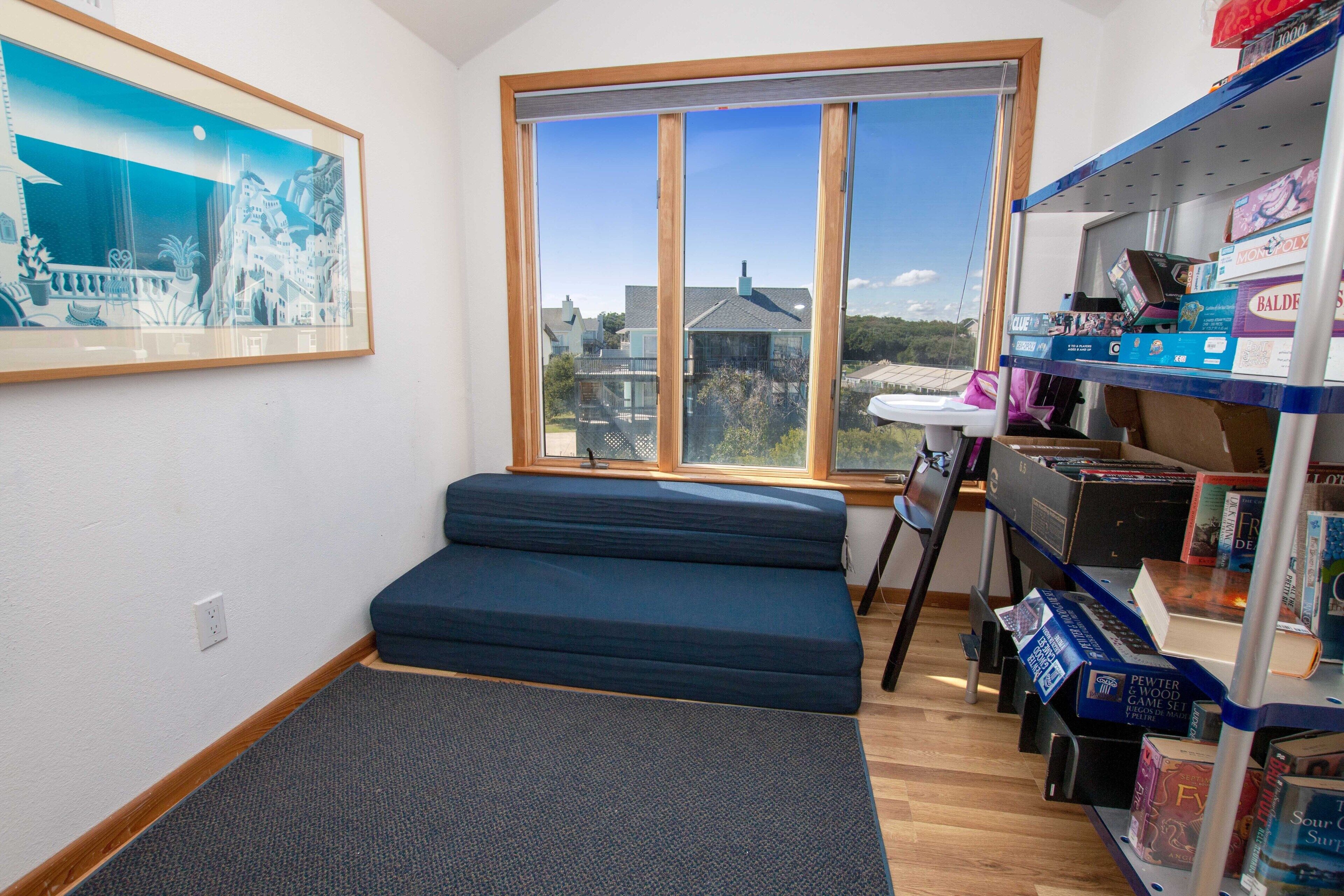 A room with a large window, a blue sofa, a small table, and a bookshelf with board games.