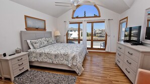 A bedroom with a bed, a dresser, a TV, a ceiling fan, and a view of the outside. - Semi-Oceanfront, Private Pool, Hot Tub, Close to Beach Access, GF2, Touch of Grey (Duck)