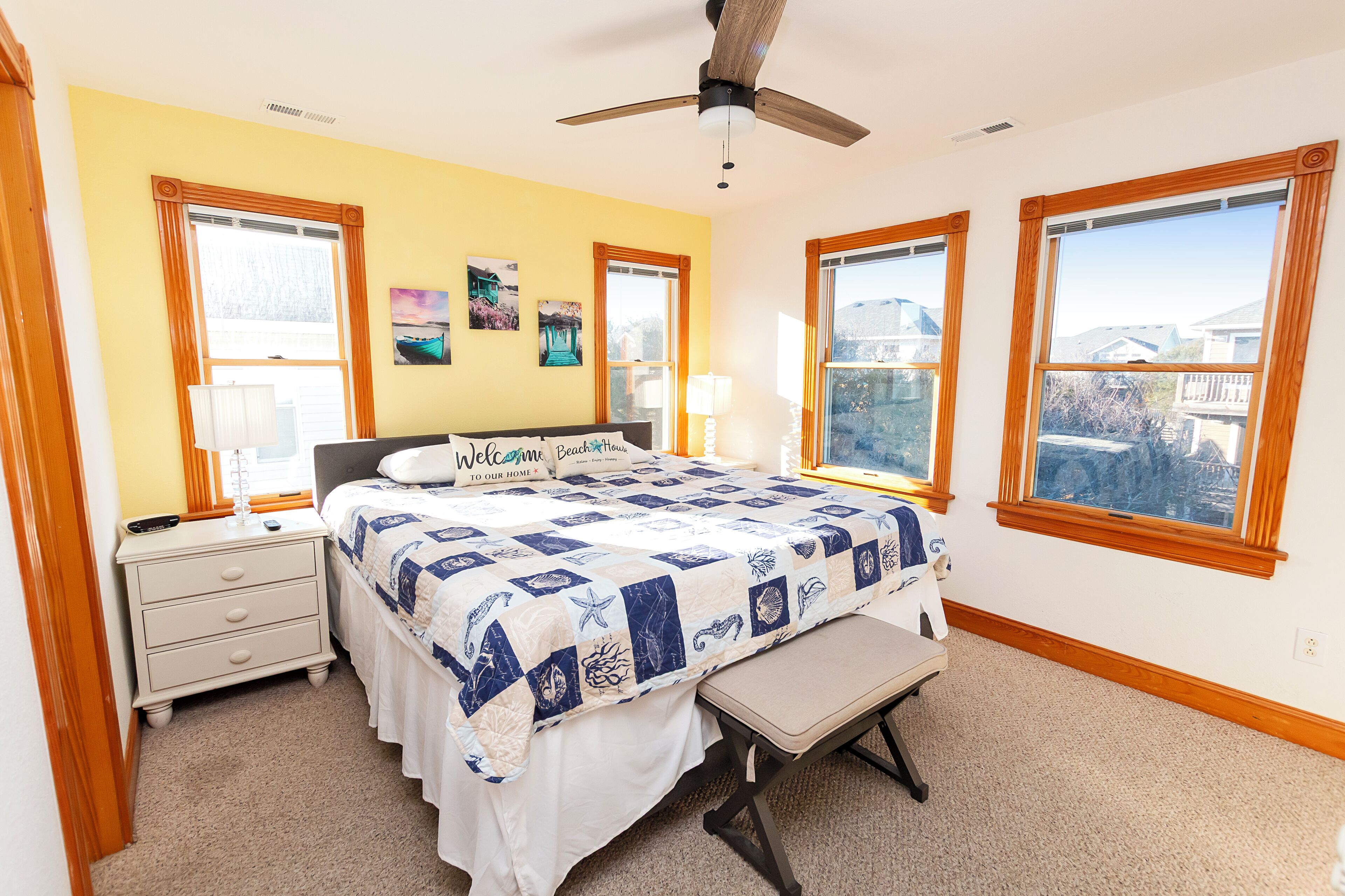 A bedroom with a bed, bedside tables, a bench, and large windows with wooden frames.