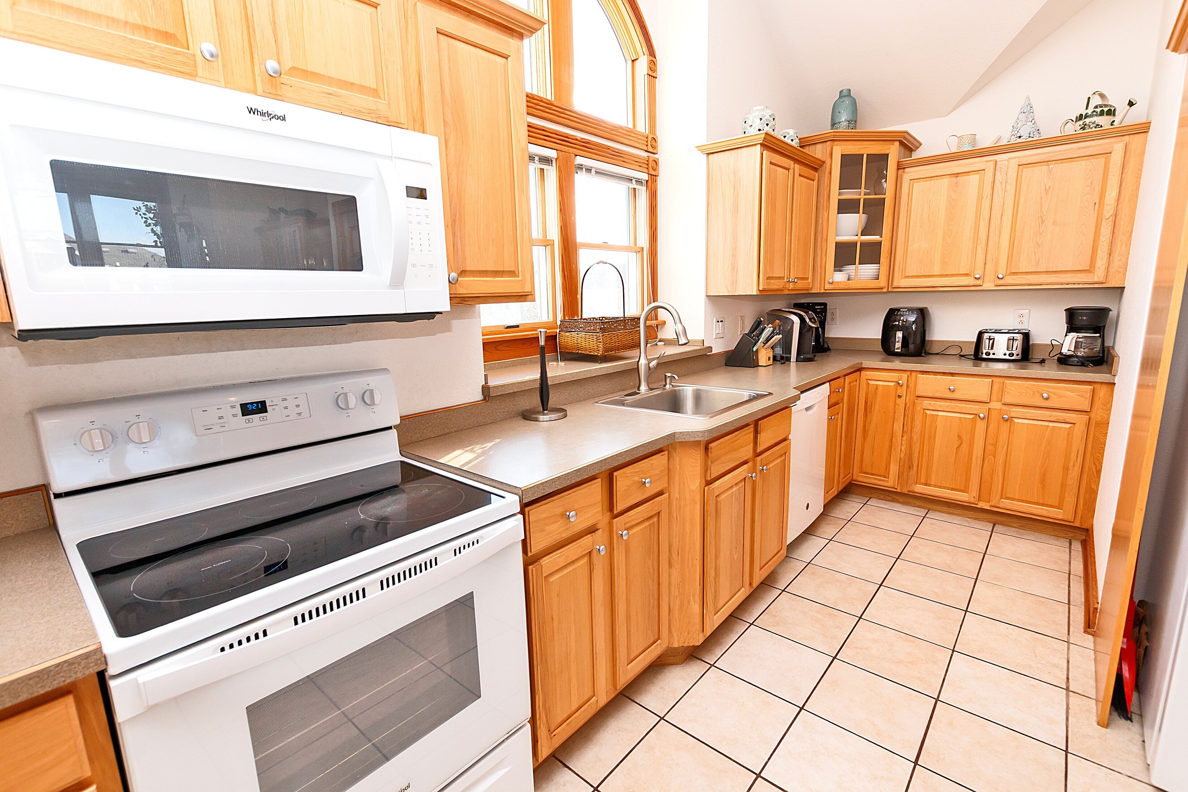 A kitchen with wooden cabinets, a white microwave, a stove, and a sink.