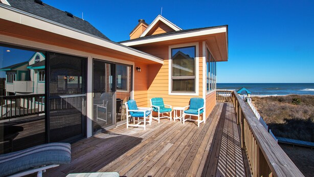 A wooden deck with outdoor seating, a glass door entrance, and a view of the ocean.