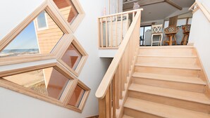 A staircase with wooden steps and a wooden railing, leading to a room with a view of the beach.