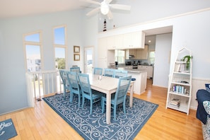 A dining area with a table and chairs, a kitchen in the background, and a bookshelf with books. - Oceanside, Close to the Beach, Private Pool, Hot Tub! 740, Wild Horses (Corolla)