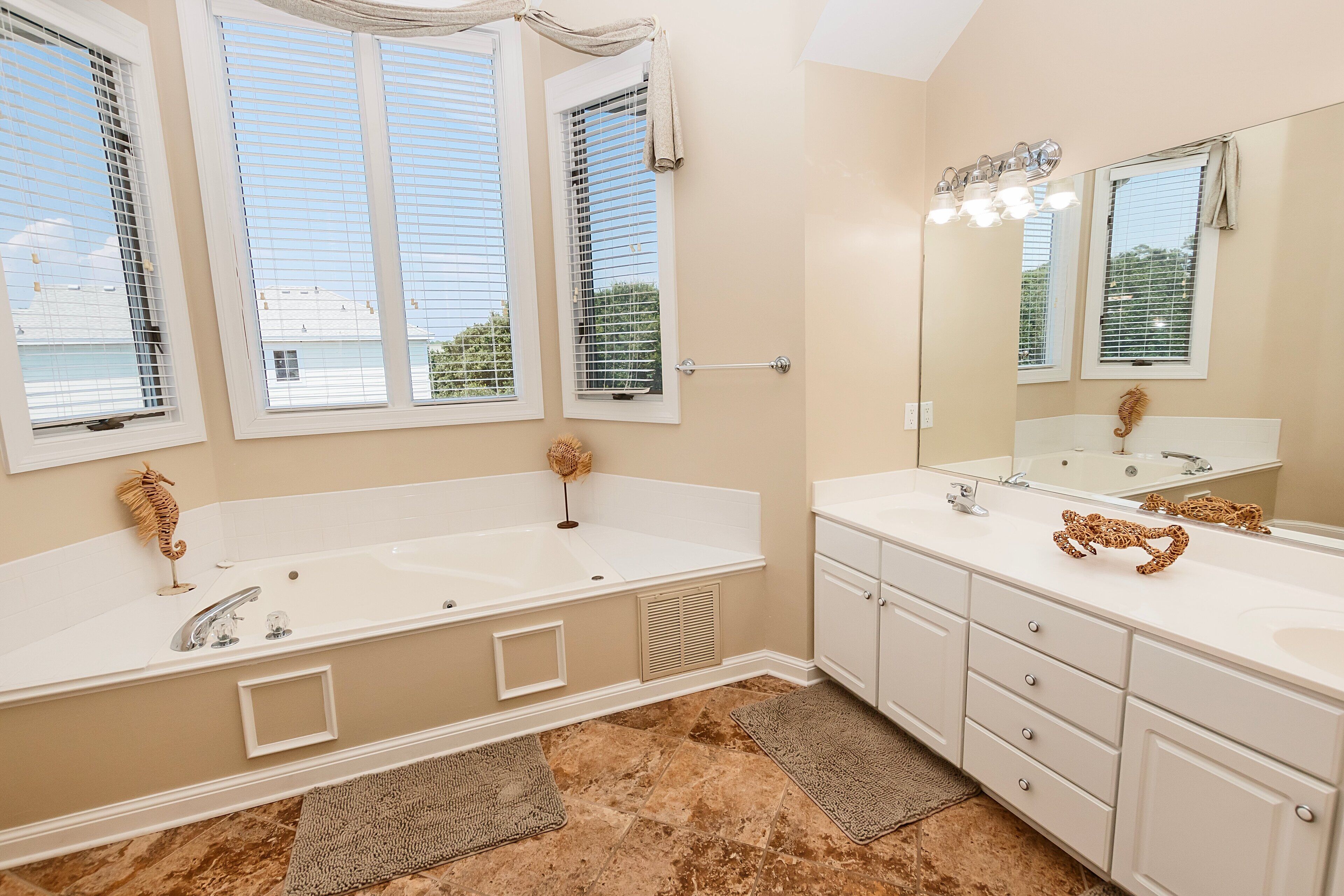 A bathroom with a large bathtub, two sinks, a vanity with drawers, a mirror, and a window with blinds.