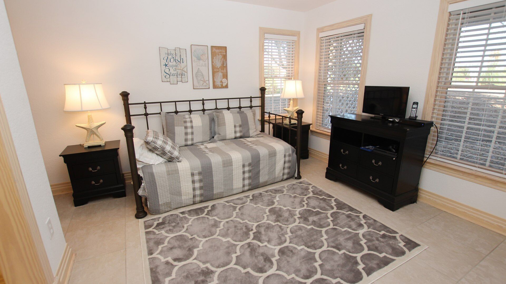 A bedroom with a bed, bedside tables, a TV stand, and decorative wall art.