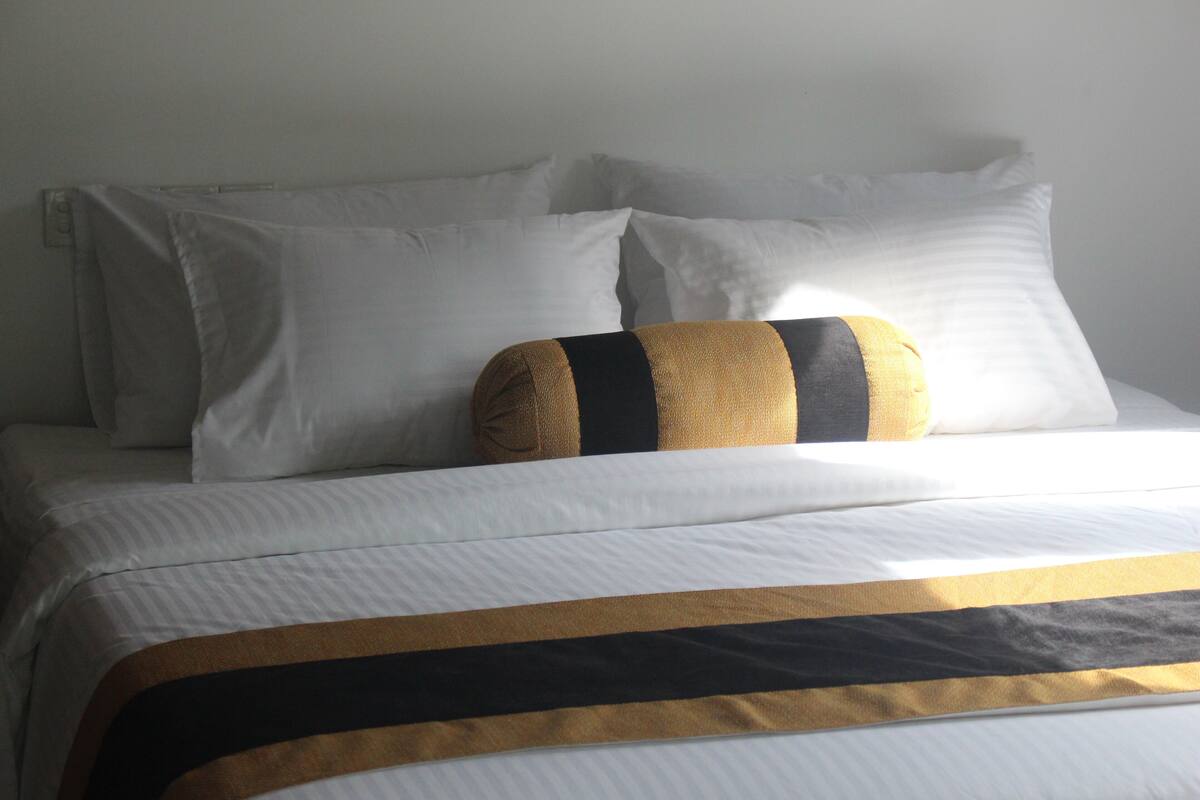 Una cama con ropa blanca y una almohada decorativa con rayas negras y doradas.