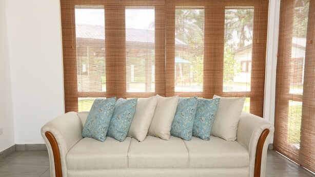 A beige sofa with patterned cushions in a room with large windows and a patterned rug. - JAS Residence Pool Villa (Divulapitiya)
