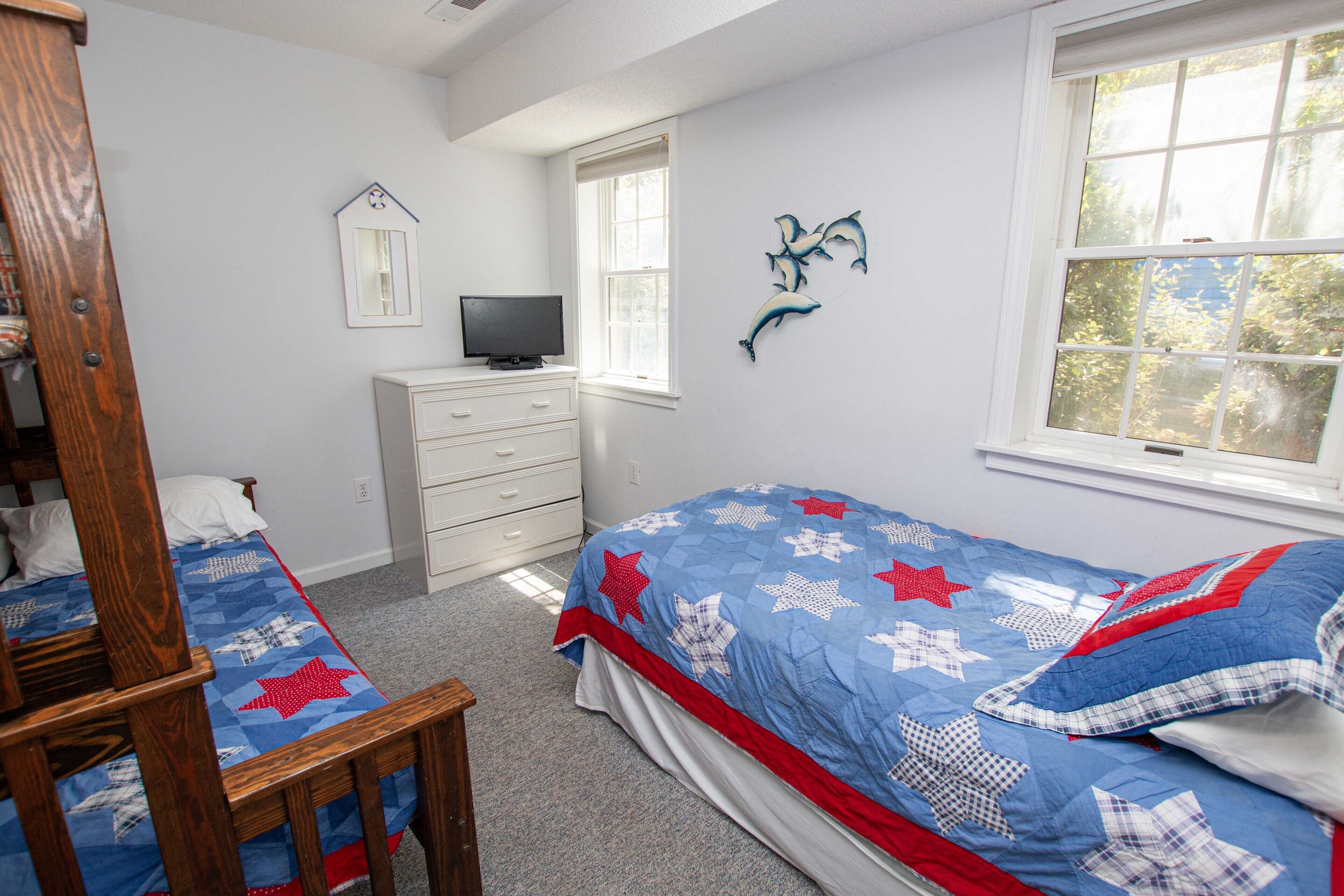Un dormitorio con cama, cómoda, televisor y ventana.
