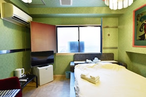A hotel room with a bed, a desk with a television, a window with a city view, and an air conditioning unit. - Hotel SAN MARCO (Tokyo)