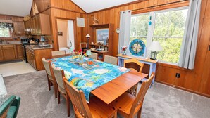 A wooden interior with a dining table, chairs, a kitchen area, and a large window with curtains. - Oceanside, Private Pool, Hot Tub, Screened Porch, WC940, Whalin (Corolla)