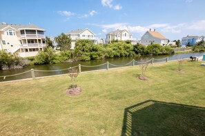 A residential area with houses along a river, a grassy lawn, and a rope barrier. - Oceanside, Hot Tub, Private Pool, Community Amenities, BU3, Tangerine Dream (Corolla)