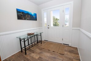A hallway with a glass-top table, a door with a window, and a painting of an underwater scene. - Oceanside, Hot Tub, Private Pool, Community Amenities, BU3, Tangerine Dream (Corolla)