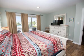 A bedroom with a large bed, a dresser, a television, and a balcony with curtains. - Oceanside, Hot Tub, Private Pool, Community Amenities, BU3, Tangerine Dream (Corolla)