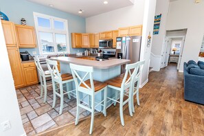 A modern kitchen with wooden cabinets, a central island with bar stools, a refrigerator, and a microwave.