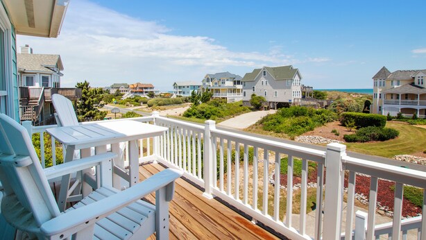 A wooden deck with white railings, a view of houses, and a clear sky. - Semi-Oceanfront, Private Pool, H Tub, Pool Table, WL864, Porch Coffee Paradise (Corolla)