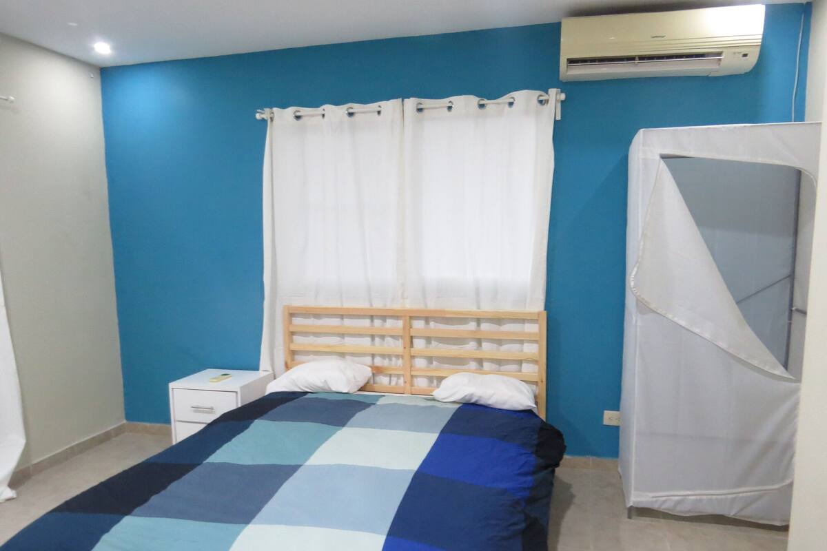 Une chambre à coucher avec un lit, une table de chevet, un rideau blanc et une moustiquaire blanche.