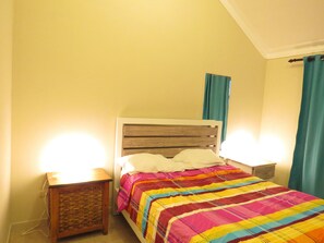 Un dormitorio con una cama, dos mesitas de noche, un cabecero de madera y una ventana con cortinas.