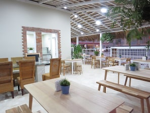 Un restaurante con mesas y sillas de madera, una pared de ladrillo con un espejo, y un techo de paja.