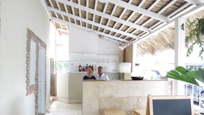 A kitchen with a thatched roof, a brick wall, and a counter with stools. - Bohio Punta Cana (Punta Cana)