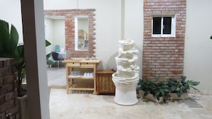 A room with a brick wall, a white pedestal fountain, a wooden desk with drawers, and a potted plant. - Bohio Punta Cana (Punta Cana)