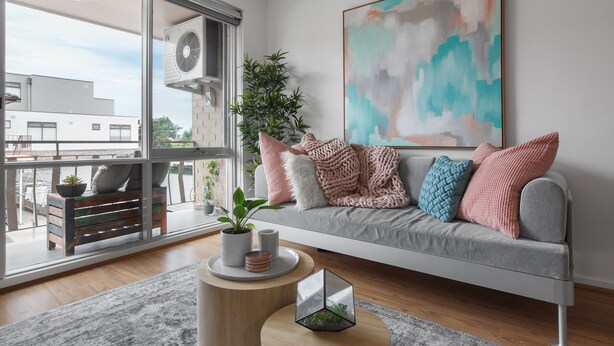 A modern living room with a grey sofa, a large abstract painting, and a potted plant. - Heart of Ormond Apartment  by Ready Set Host (Ormond)