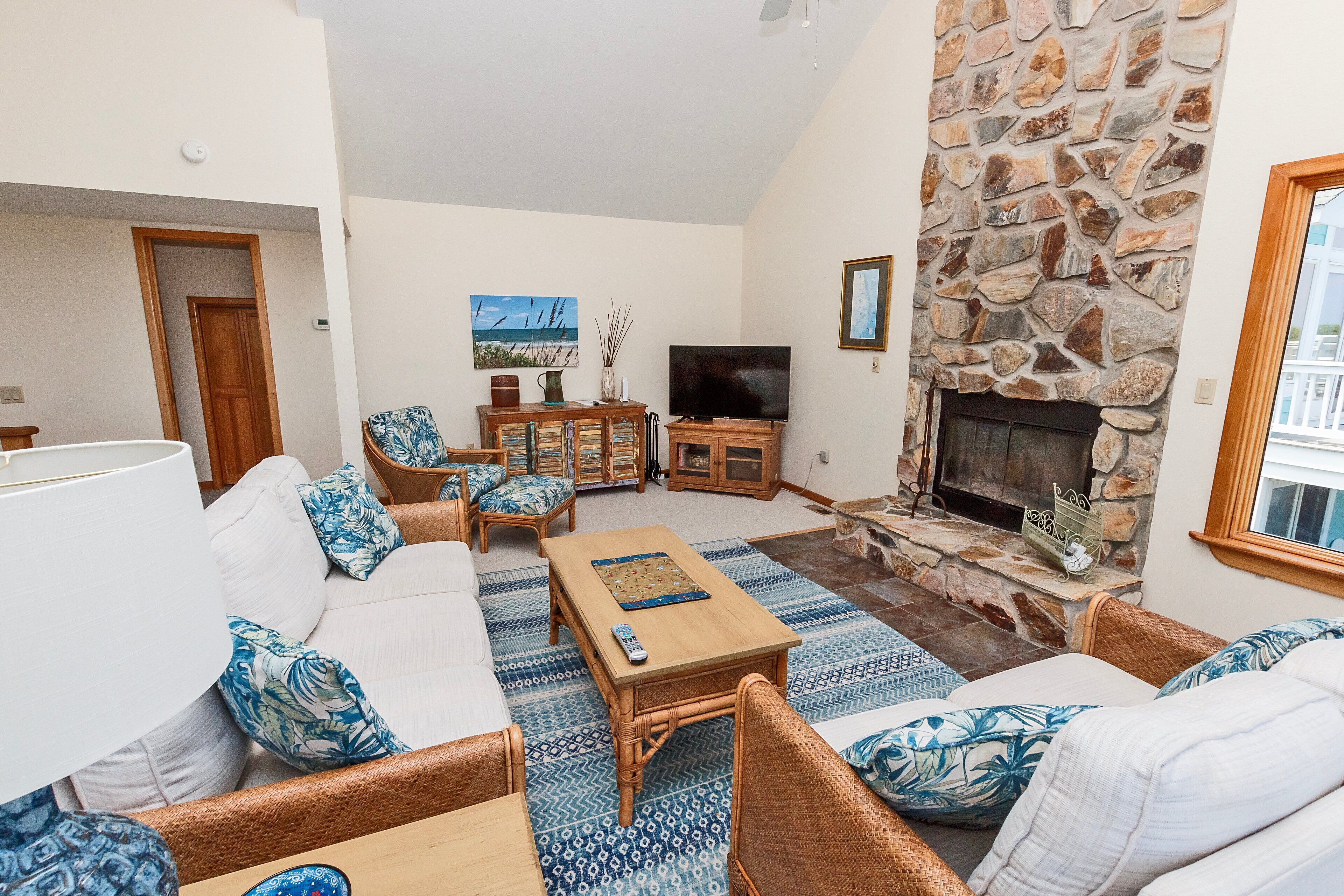 A living room with a stone fireplace, a television, and a sofa with patterned cushions.