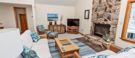 A living room with a stone fireplace, a television, and a sofa with patterned cushions.