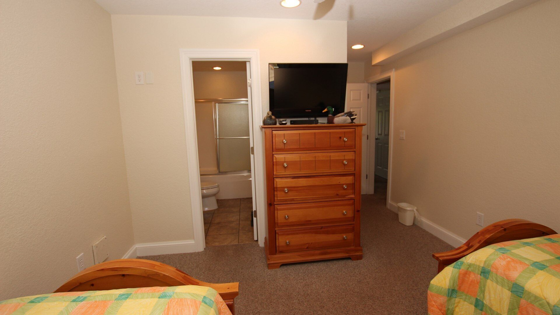 Un dormitorio con un aparador de madera, un televisor y un baño visible a través de una puerta abierta.