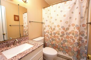 A bathroom with a granite countertop sink, a white toilet, and a shower curtain with a shell pattern. - Oceanside, Sun Deck, Close to beach! KH106, Annie Oakley (Kitty Hawk)
