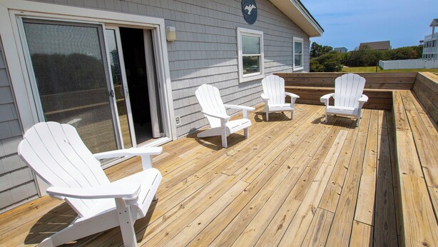 Une terrasse avec des chaises Adirondack blanches et un revêtement de sol en bois.