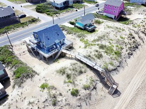 Uma casa à beira-mar com telhado azul, um deque e uma escadaria dando acesso à praia.