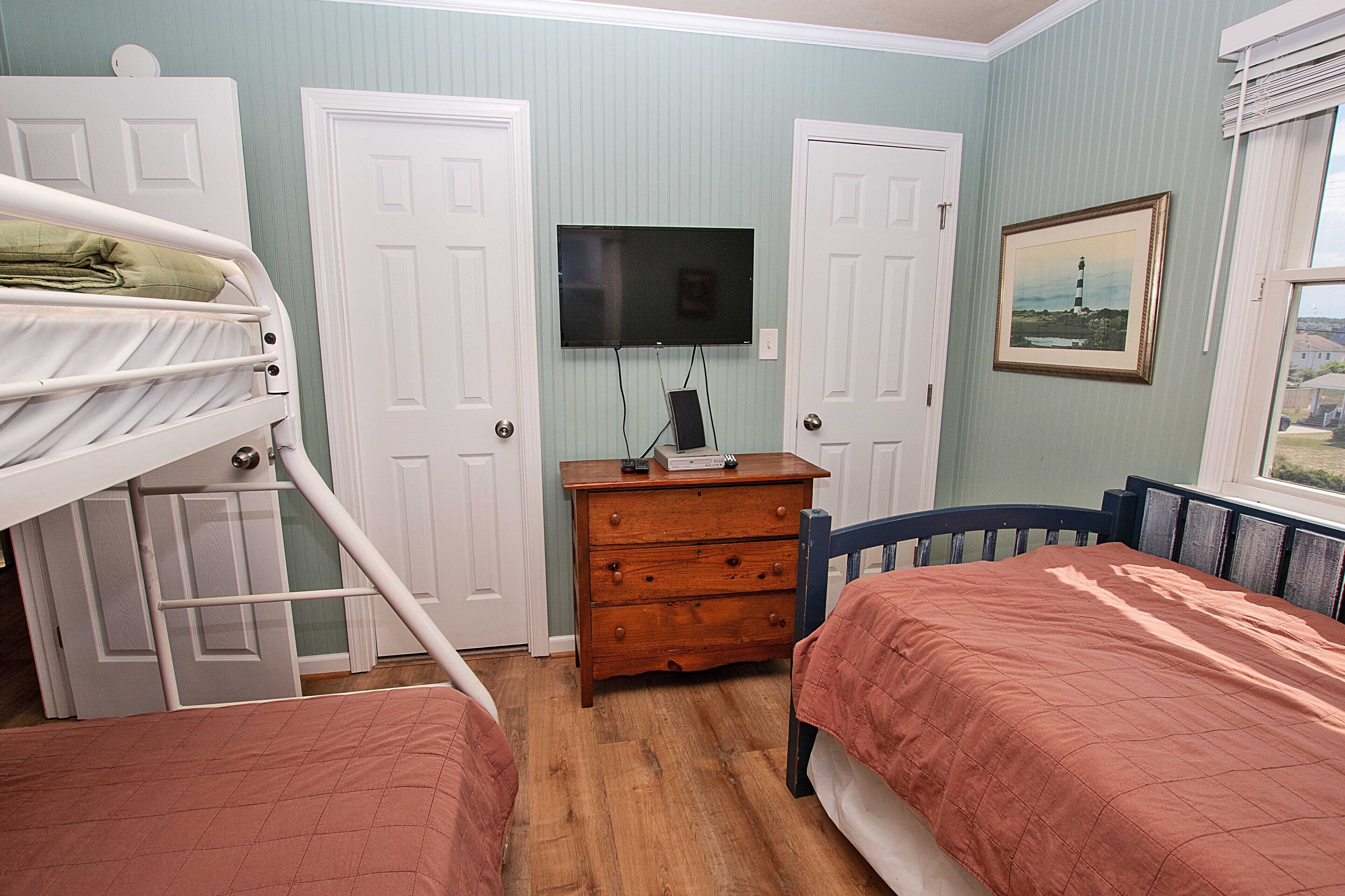Um quarto com beliches, cômoda, televisão e um quadro na parede.