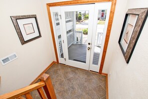 A hallway with a wooden handrail, a white door with glass panels, and a tiled floor.