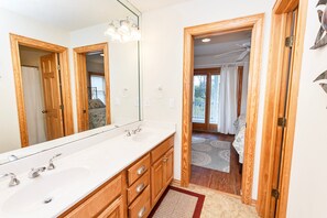 A bathroom with a large mirror, two sinks, wooden cabinets, and a view of a balcony through an open door. - Semi-Soundfront, Rec Room, Private Pool, Hot Tub, 566, Finnegans Wake (Corolla)