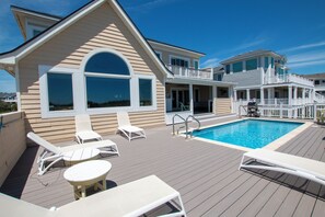 A poolside area with lounge chairs, a pool, and a building with a balcony.