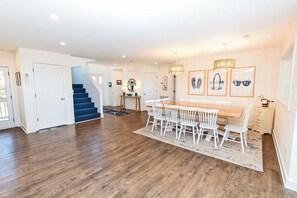 A spacious living area with a wooden floor, a dining table with chairs, a staircase, and a hallway leading to another room. - OCEANFRONT, Ocean Views, Private Pool, Rec Room, 230, Long Weekends (Corolla)