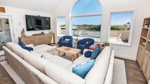 A spacious living room with a large sofa, two armchairs, a coffee table, and a TV. There are large windows offering a view of the beach and ocean. - OCEANFRONT, Ocean Views, Private Pool, Rec Room, 230, Long Weekends (Corolla)