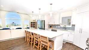 A modern kitchen with a large island, bar stools, white cabinetry, and a view of the outdoors. - OCEANFRONT, Ocean Views, Private Pool, Rec Room, 230, Long Weekends (Corolla)